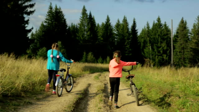 Two-small-girls-with-bikes-walking-along-the-rural-road