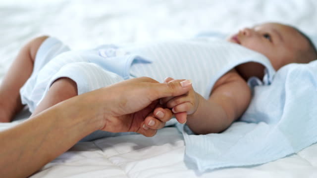 Baby-Hand-halten-Finger-der-Mutter-auf-einem-Bett