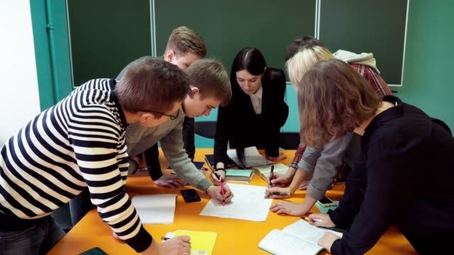Group-of-young-students-making-task-under-teacher's-supervision