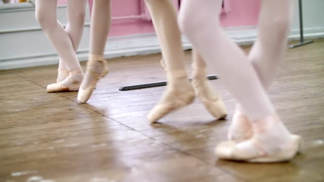 in-ballet-hall,-Young-ballerinas-perform-pas-echappe-in-pointe-shoes,-goes-up-on-toes,-close-up