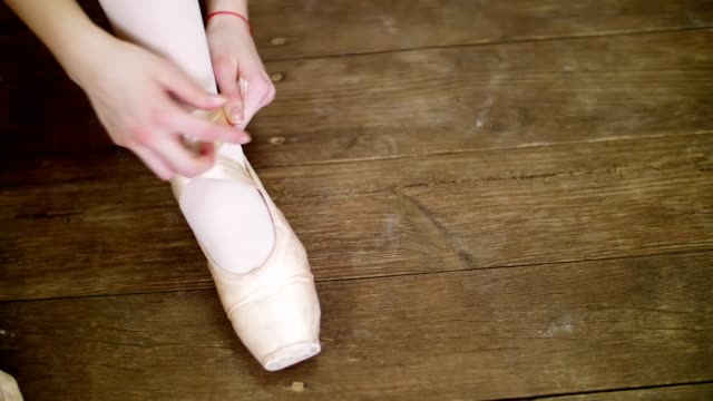 close-up,-ballerinas-change-their-shoes-into-special-ballet-shoes,-pointe-shoes,-lace-with-ballet-ribbons,-on-an-old-wooden-floor,-in-ballet-class