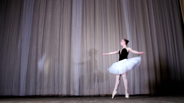 ballet-rehearsal,-on-the-stage-of-the-old-theater-hall.-Young-ballerina-in-white-ballet-tutu-and-pointe-shoes,-dances-elegantly-certain-ballet-motion,-glissad-en-tornant