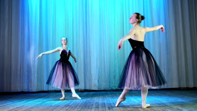 ballet-rehearsal,-on-the-stage-of-the-old-theater-hall.-Young-ballerinas-in-lilac-black-elegant-dresses-and-pointe-shoes,-dance-elegantly-certain-ballet-motion,-arabesque