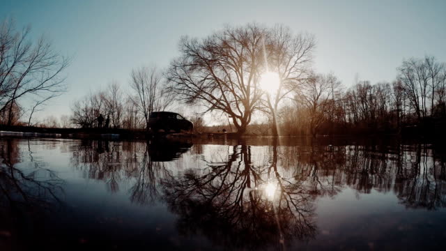 Reflexion-der-Bäume-ohne-Blätter-auf-Zweigen-im-Frühjahr-Hochwasser-im-Fluss-bei-Sonnenuntergang