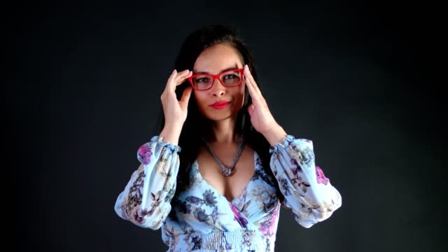 portrait-of-a-sexy-brunette-woman-with-red-lips-who-eroticly-and-playfully-tries-on-stylish-glasses,-spectacles-and-looking-sexually-at-camera,-posing-in-studio.-dark-gray-background