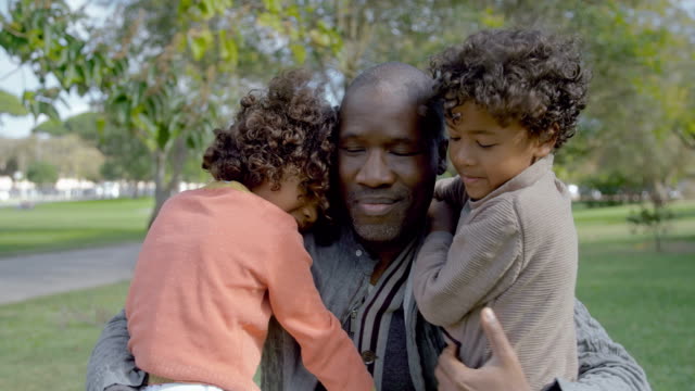 African-American-dad-abrazando-a-niños-rizados-en-el-parque-de-verano