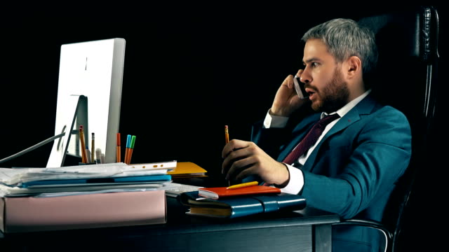 Angry-bearded-businessman-having-emotional-stressful-conversation-on-his-cell-phone.-Black-background.-FullHD-video