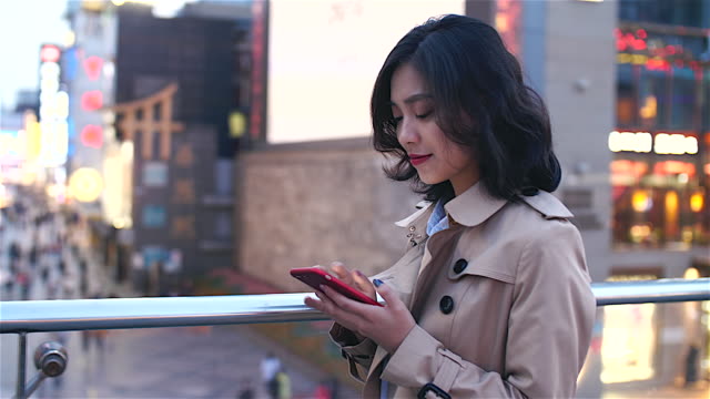 Pretty-happy-young-asian-woman-using-mobile-phone--in-the-Chinese-city-of-Chengdu-while-walking-on-the-overpass-with-busy-street-in-the-background