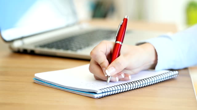 Office-Worker-Hand-Schreiben-von-Notizen-in-einem-Notizbuch-auf-einem-Schreibtisch