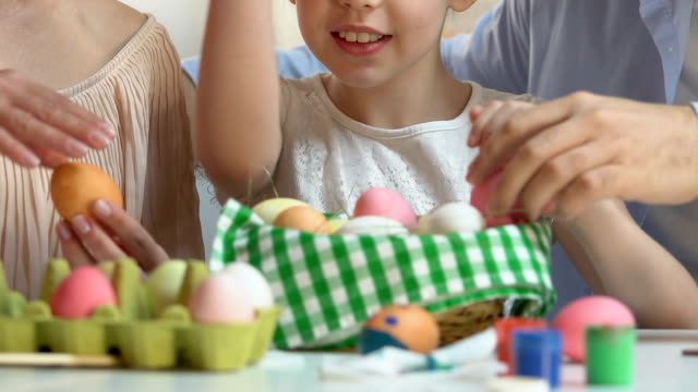 Family-putting-colored-eggs-into-basket,-preparing-for-Easter-fest,-traditions