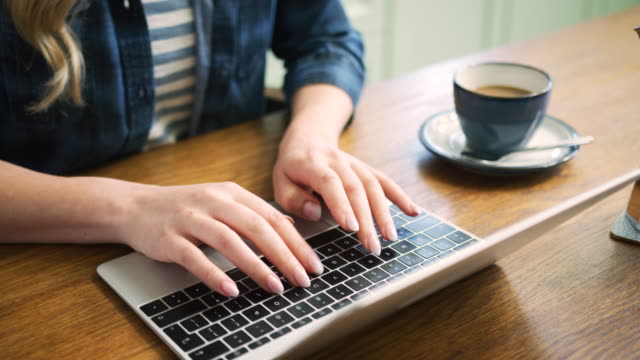 Mujer-escribiendo-en-la-computadora-portátil-y-tomando-café-en-la-mesa