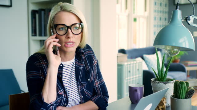 Attractive-Blond-Businesswoman-Talking-On-Smart-Phone-In-Home-Office