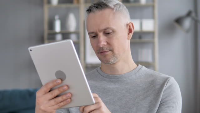 Graue-Haare-Mann-mit-Tablet-am-Arbeitsplatz