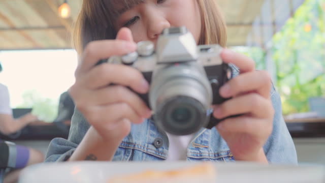 Food-blogger-Asian-woman-using-camera-for-photo-dessert,-bread-and-drink-while-sitting-on-table-in-cafe.-Lifestyle-beautiful-women-relax-at-coffee-shop-concepts.