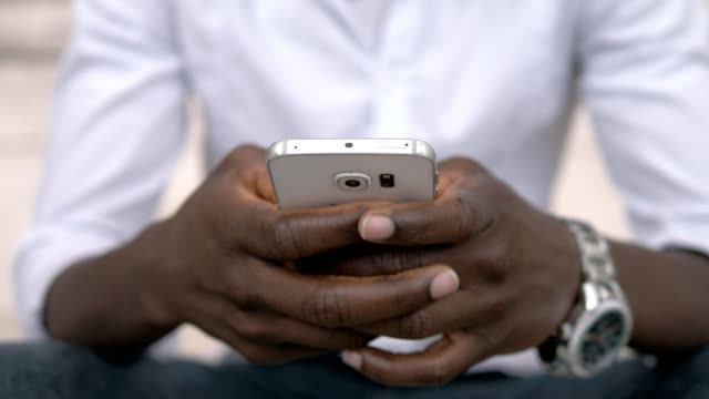 Die-Hände-des-afrikanischen-Amerikaners-tippen-auf-smartphone-outdoor