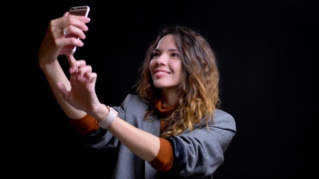 Closeup-portrait-of-positive-caucasian-young-female-taking-selfies-on-the-phone-smiling-and-posing