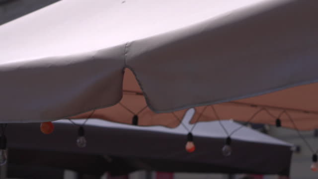 Sunshade-over-the-tables-of-the-summer-open-area-of-the-restaurant-on-the-city-street.-Close-up
