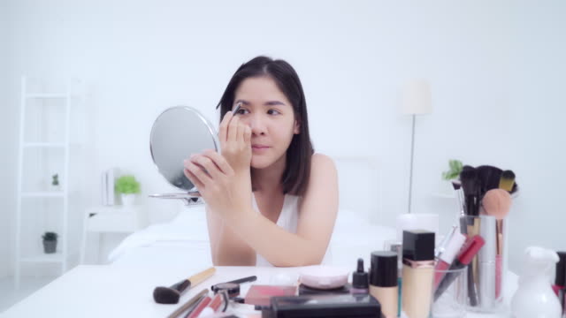 Beauty-Blogger-präsentieren-Beauty-Kosmetik-sitzen-in-der-Frontkamera-für-die-Aufnahme-von-Video.-Glückliche-schöne-junge-asiatische-Frau-verwenden-Kosmetik-Bewertung-Make-up-Tutorial-übertragen-Live-Video-zu-sozialen-Netzwerken.