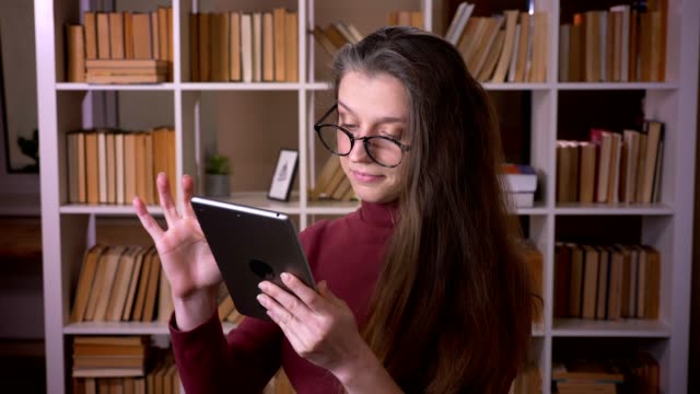 Nahaufnahme-Porträt-der-jungen-kaukasischen-Studentin-in-Brille,-die-auf-dem-Tablet-drinnen-in-der-College-Bibliothek-drinnen-tippt