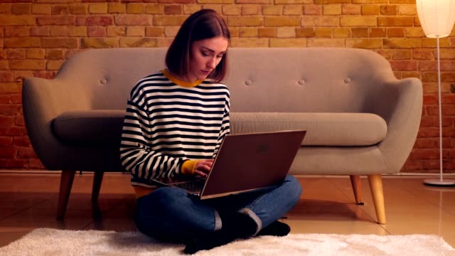 Closeup-portrait-of-young-pretty-female-studying-online-the-laptop-sitting-on-the-floor-in-a-cozy-apartment-indoors