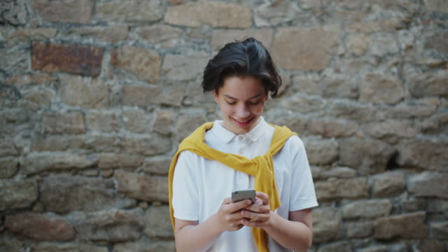 Glücklicher-Teenager-mit-modernen-Smartphone-im-Freien-berühren-Bildschirm-lächelnd