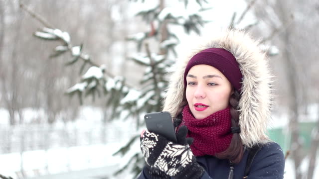 Schöne-junge-Mädchen-flippt-durch-soziale-Netzwerke-in-ihrem-Smartphone-beim-Gehen-in-einem-Winterpark.