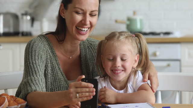 Glückliche-Mama-und-Kind-Tochter-lachen-mit-dem-Smartphone-zu-Hause