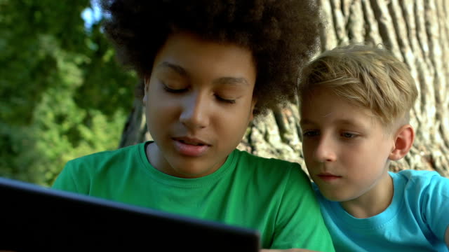 Male-friends-scrolling-tablet-application-sitting-outdoors-together,-technology