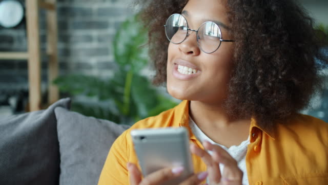 Glücklicher-afroamerikanischer-Teenager-mit-Smartphone-zu-Hause-lachen