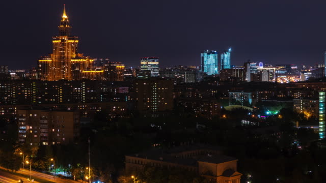Timelapse-architecture-night-city-on-dark-sky-landscape.-Night-illumination-in-modern-city.-Moon-moving-in-cloudy-sky-over-dark-city.-Night-city-landscape-from-drone