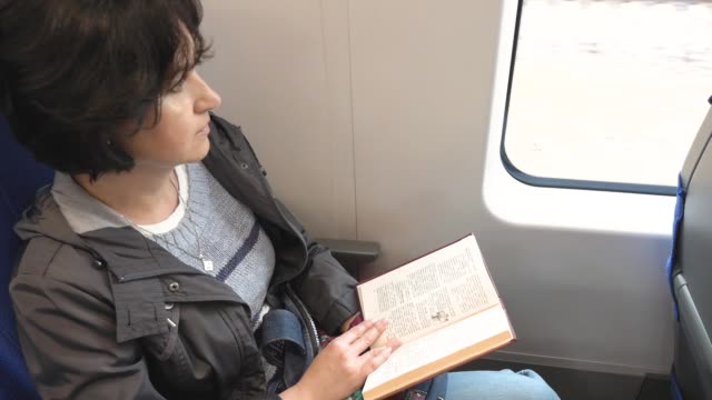 Caucasian-woman-rides-a-train-sitting-by-the-window-with-an-open-book