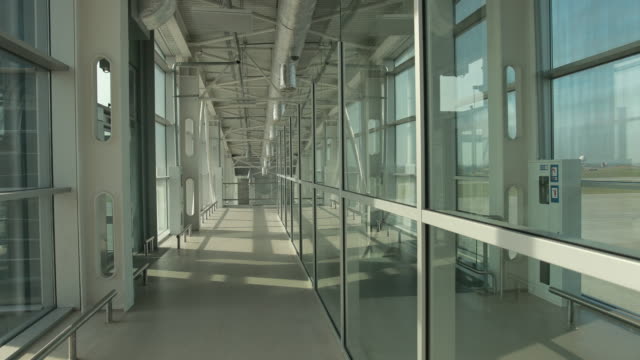 Stylish-glass-corridor-in-airport-terminal-to-runway-with-planes.