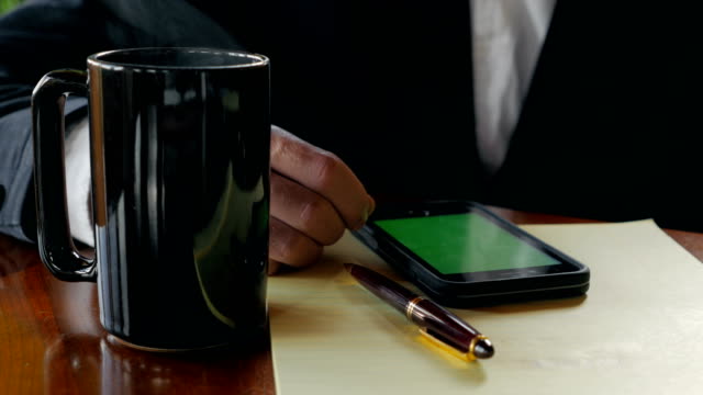 Primer-plano-del-hombre-de-negocios-bebiendo-café-con-pantalla-verde-del-teléfono-móvil