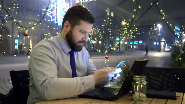 Focused-businessman-writing-on-smartphone,-at-night,-in-cafe,-christmas