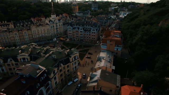 Drohne-Kamera-bewegt-sich-unter-den-Dächern-von-Gebäuden-auf-die-alten-europäischen-Gassen-mit-bunten-Häusern-und-Fußgänger-bei-Sonnenuntergang-4K