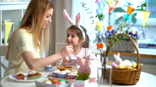 Young-mother-and-her-daughter-wearing-Bunny-ears-cooking-Easter-cupcakes
