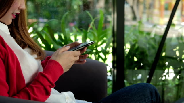junge-Frau-trägt-rote-Strickjacke-mit-Smartphone-für-social-Networking.-Mädchen-Textmitteilung-auf-Antrag-im-Handy-zu-schreiben.-Technik,-Kommunikation,-Menschen,-Lifestyle-Konzept