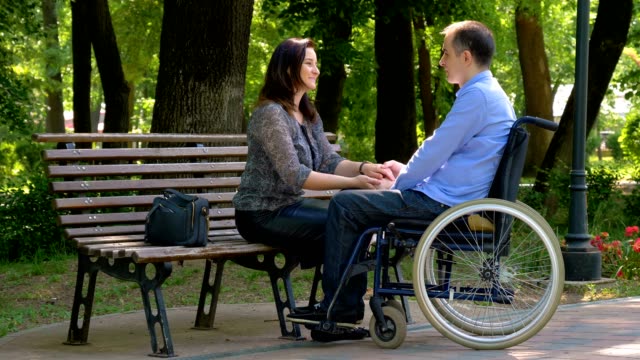 Junger-Mann-im-Rollstuhl-im-Gespräch-mit-seiner-Frau-im-park
