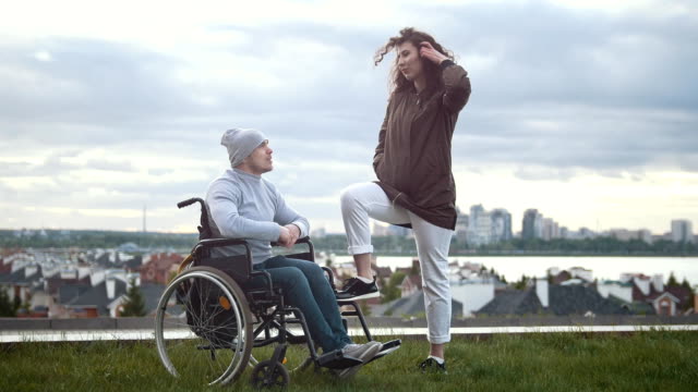 Happy-disabled-man-in-a-wheelchair-embraces-with-young-woman-outdoors