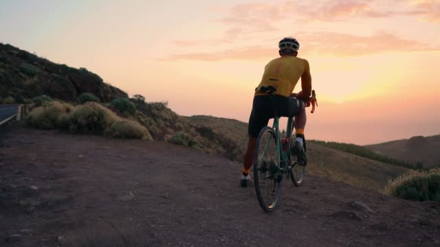 Cyclist-sitting-on-a-bike-taking-pictures-on-a-smartphone-for-social-networking-mountain-landscape-at-sunset.-Slow-motion