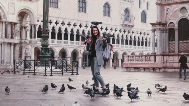 Happy-excited-attractive-tourist-woman-with-pigeons-sitting-on-her-arm-and-head-at-city-square-in-Venice-slow-motion.