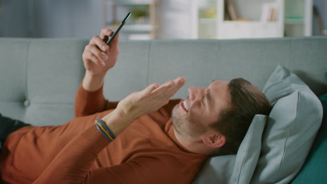 Man-at-Home-Lying-on-Sofa-Does-Video-Call-on-Smartphone.