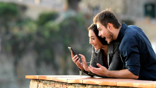 Surprised-couple-checking-phone-content-in-a-balcony