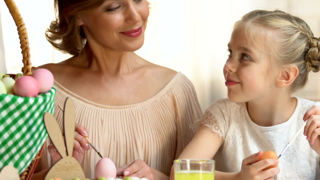Beautiful-mom-and-daughter-preparing-for-Easter-painting-eggs,-posing-at-camera
