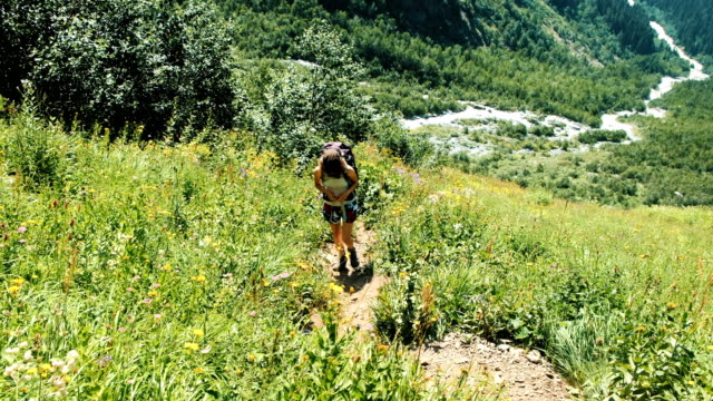 Junge-Frau-Tourist-mit-einem-Rucksack-steigt-bergauf-im-Hintergrund-von-einer-wunderschönen-Landschaft.-Das-Mädchen-klettert-im-Sommer-zu-Fuß