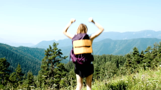 Frau-Tourist-mit-einem-Rucksack-erhebt-die-Hände-und-springt-vom-Glück-vor-dem-Hintergrund-einer-wunderschönen-Berglandschaft-während-einer-Wanderung.-Das-Konzept-der-Zielerreichung,-Erfolg-und-Sieg.