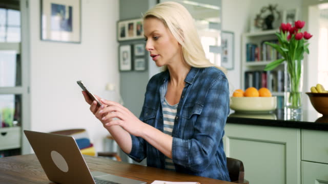 Beautiful-Blond-Woman-Typing-On-Laptop-And-Talking-On-Smart-Phone