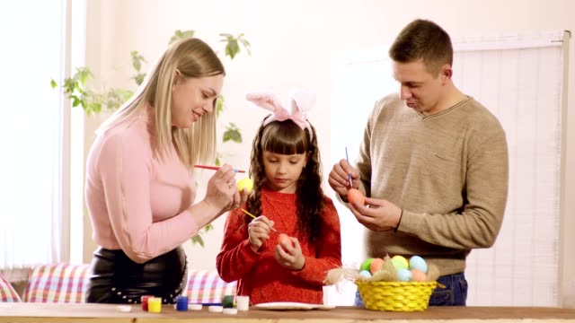 the-girl-holds-an-Easter-egg,-and-mom-and-dad-draw-on-it.