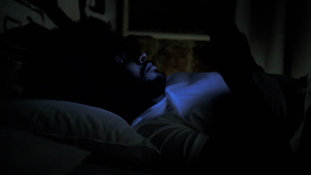 Afrikanischer-Mann-tippen-Nachricht-auf-Telefon-in-Bett-bei-Nacht