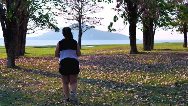 Eine-fette-asiatische-Frau,-die-abends-im-natürlichen-Sonnenlicht-joggt.
Sie-versucht,-mit-Übung-Gewicht-zu-verlieren.--Konzept-Gesundheit-mit-Bewegung.-Zeitlupe